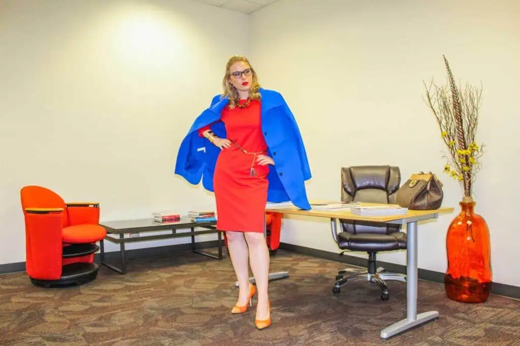 Stylish woman in a vibrant red dress and blue blazer inside a modern office space.
