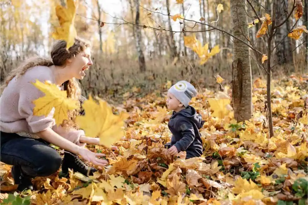 Mom tossing fall leaves while toddler watches during a playful Family Fall Photoshoot outdoors.